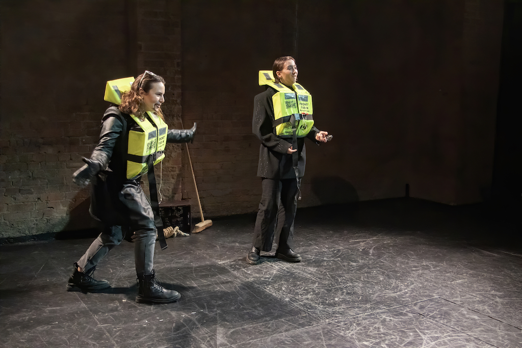 Two actors wearing neon-yellow life jackets in mid-performance.